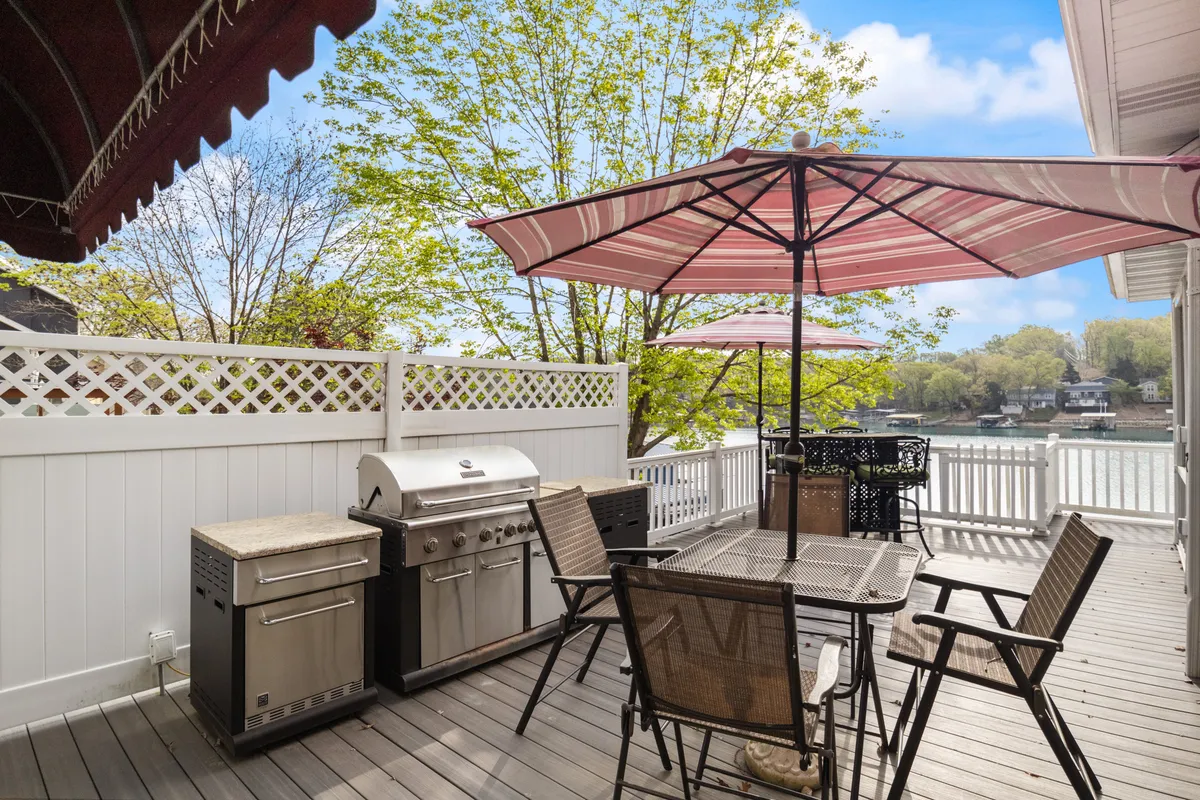The image highlights an outdoor dining area overlooking the water, complete with a grill, table and chairs, and sun umbrellas. The scene is set for relaxed social gatherings and lakeside picnics, offering partial covering for comfort and an inviting atmosphere for shared meals.