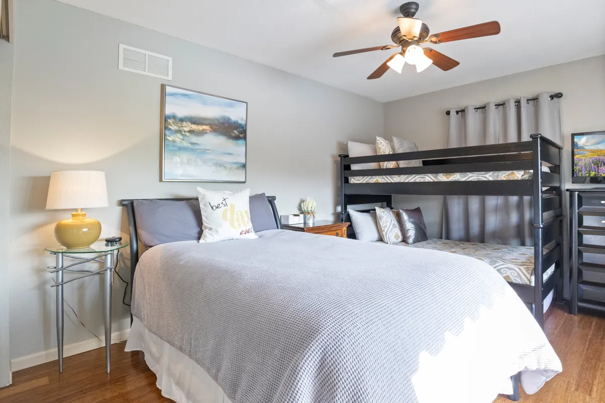 A family-friendly bedroom setup with both a bunk bed and a queen bed, complemented by artwork on the wall, a lamp, and a nightstand. The room evokes a sense of coziness and is well-suited for families or groups.