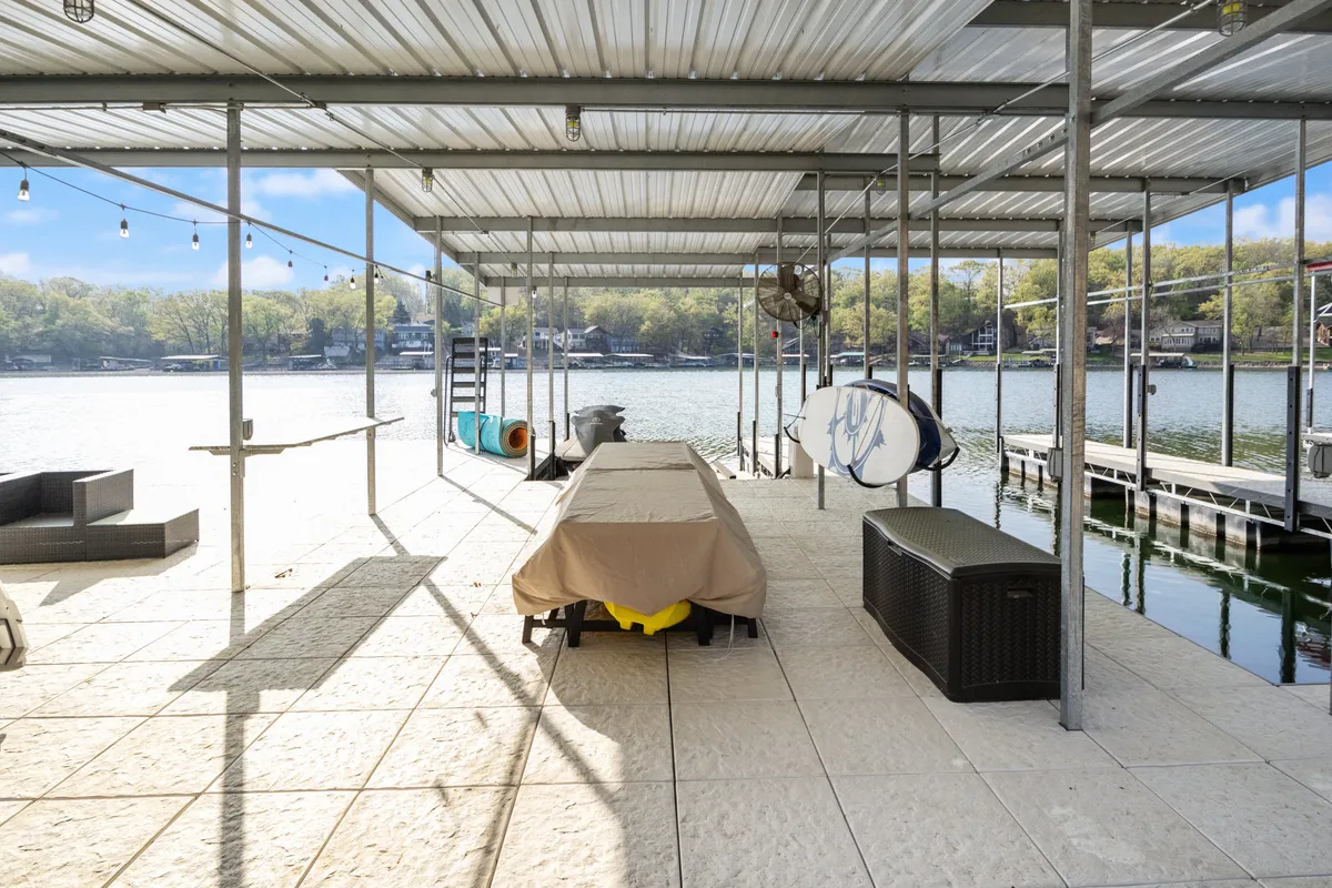 A covered table and dock area, with a surfboard propped nearby and a clear view of the water. The setup suggests readiness for group picnics, water sports, and social gatherings by the lake.