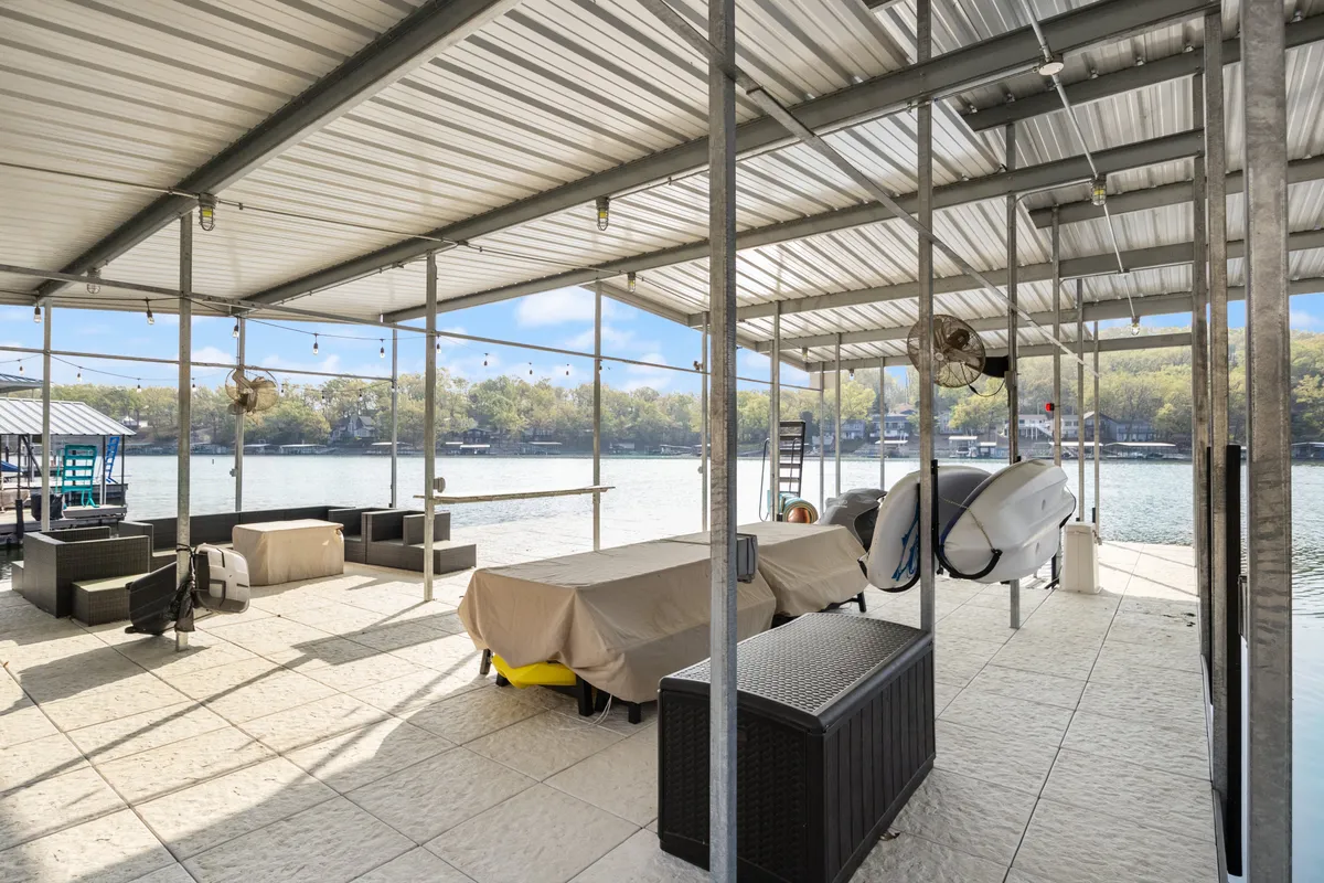 Outdoor seating is arranged beneath a covered area with lake views and a boat nearby. The scene invites both relaxation and socializing, with the calm water and comfortable furniture reinforcing an atmosphere for lingering and making memories.