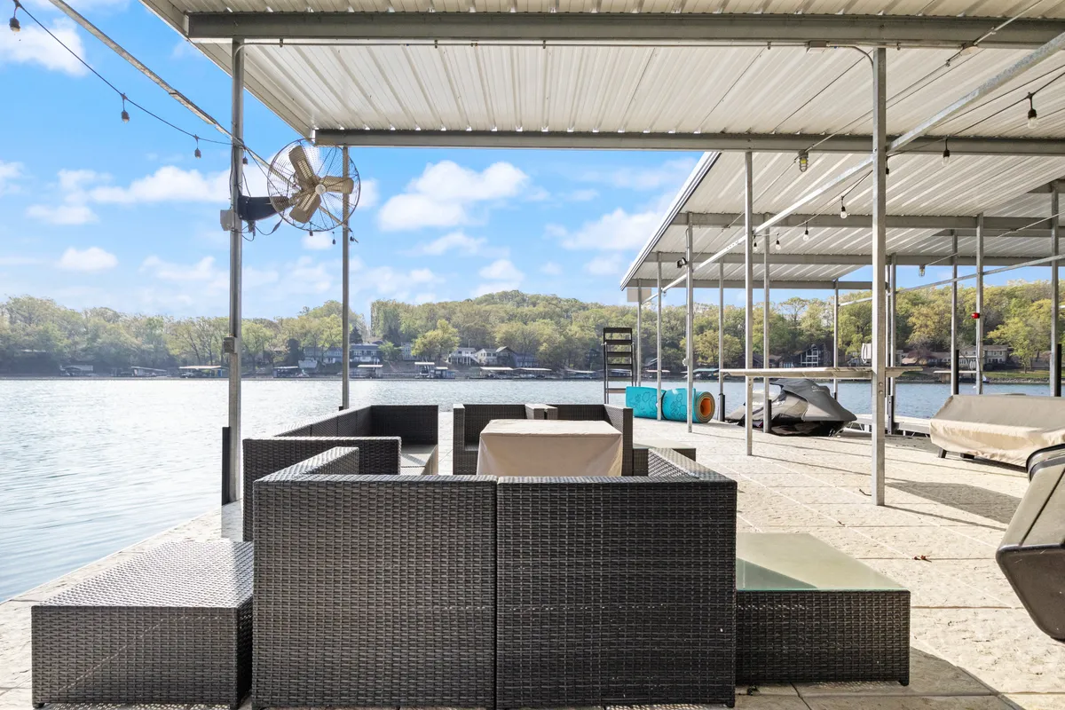 An inviting outdoor seating area overlooks the lake, with ceiling fans and decorative lights creating a tranquil ambiance. The view features the lake just steps away, ideal for launching into aquatic adventures or enjoying downtime after an active day.