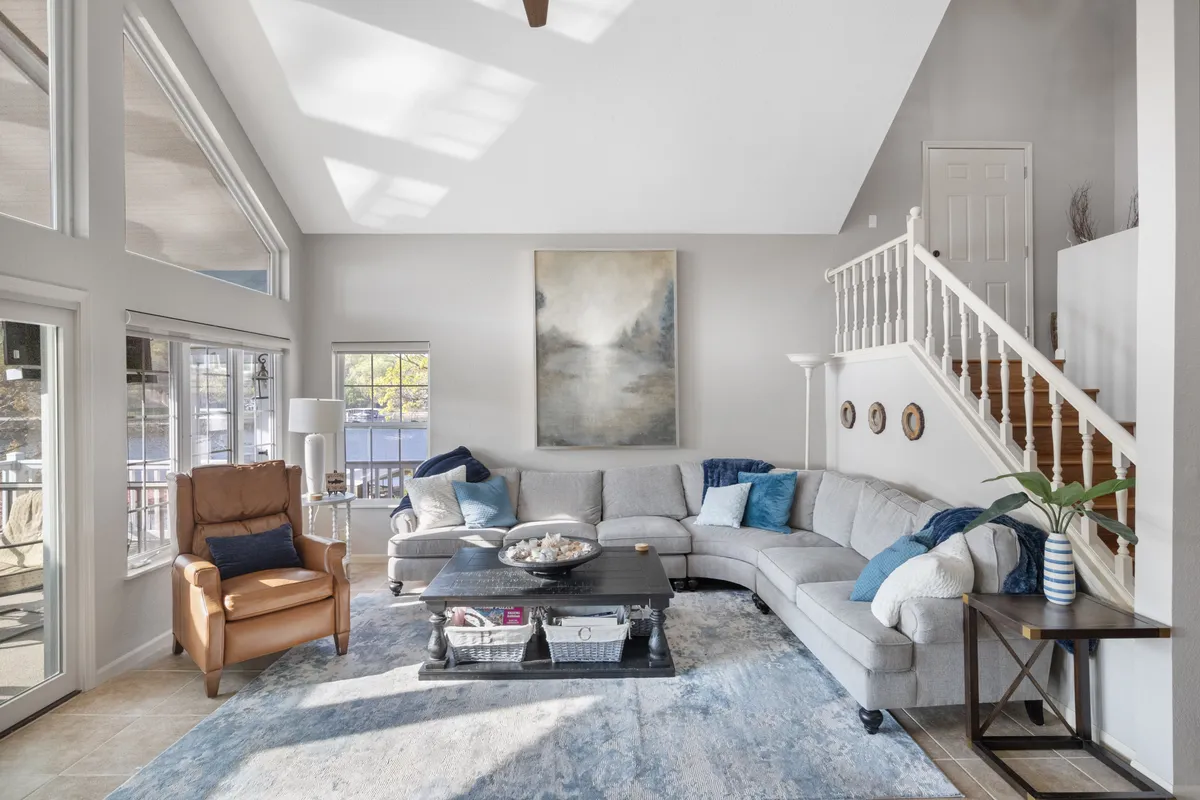 A comfortable living area with a large sectional sofa, artwork on the wall, coffee table with decorative items, and windows that flood the room with sunlight. The layout invites relaxation, conversation, and connection, embodying the spirit of family gatherings and group activities.